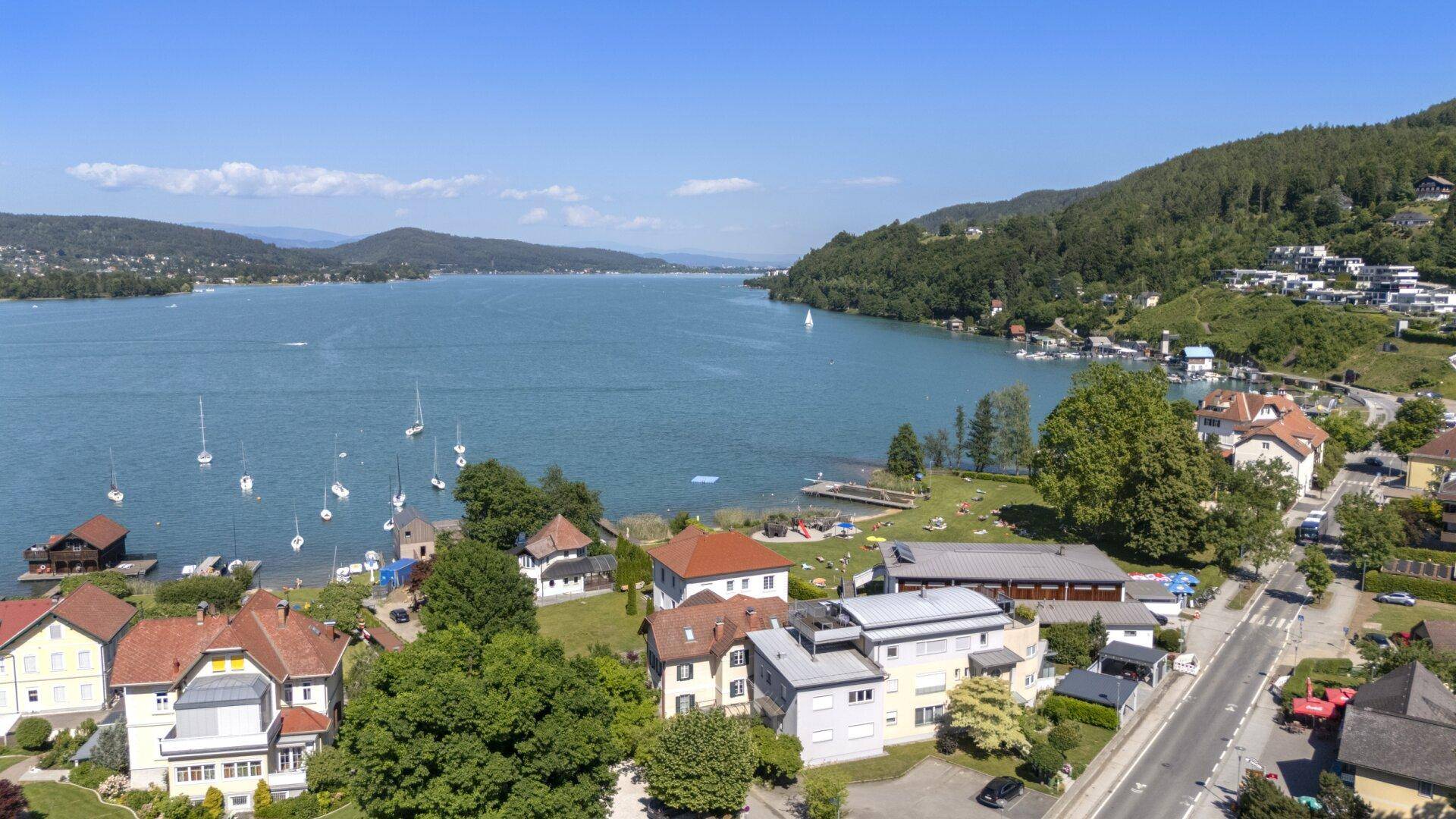 Weitläufige Luftaufnahme des Sees mit Uferbebauung und bewaldeten Hügeln.