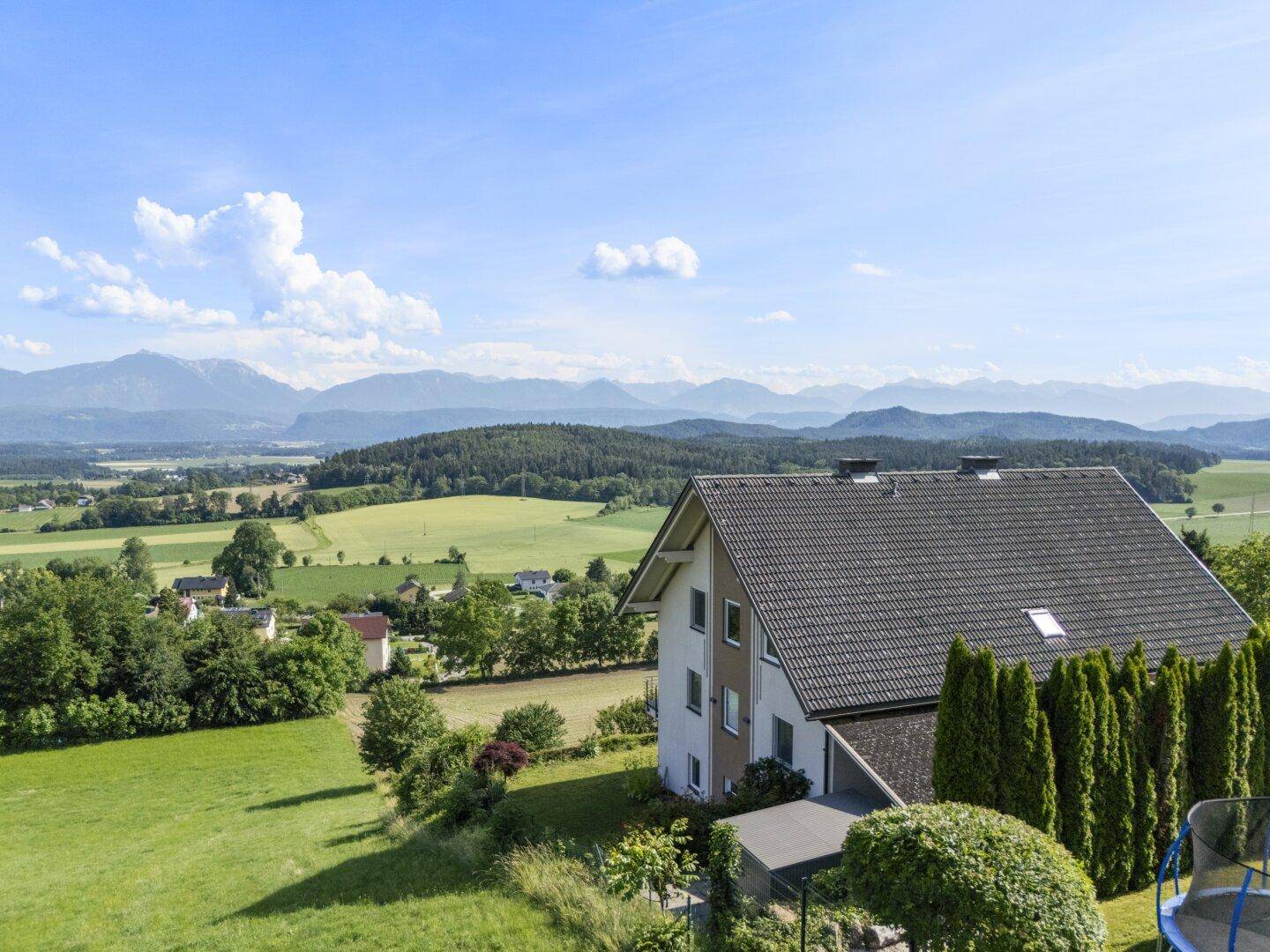 Dachansicht eines Hauses mit weitem Blick über grüne Felder und ferne Berge unter blauem Himmel.