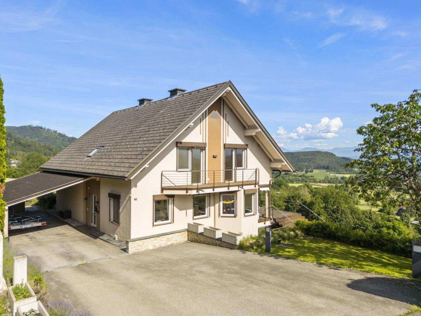 Vorderansicht des Hauses mit Carport und großzügiger Auffahrt, umgeben von grüner Landschaft.