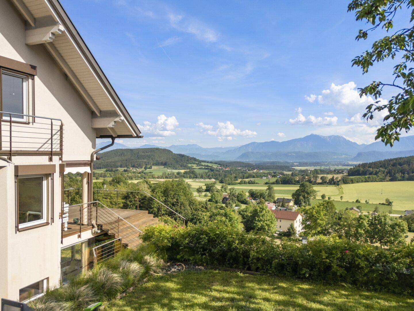 Seitenansicht des Hauses mit Balkon und weitem Blick über die grüne Landschaft und Berge.