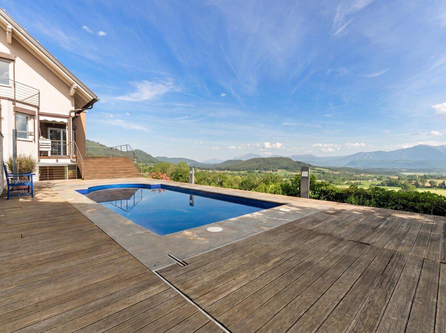 Blauer Pool mit Holzdeck und beeindruckendem Panoramablick über die weite grüne Landschaft.
