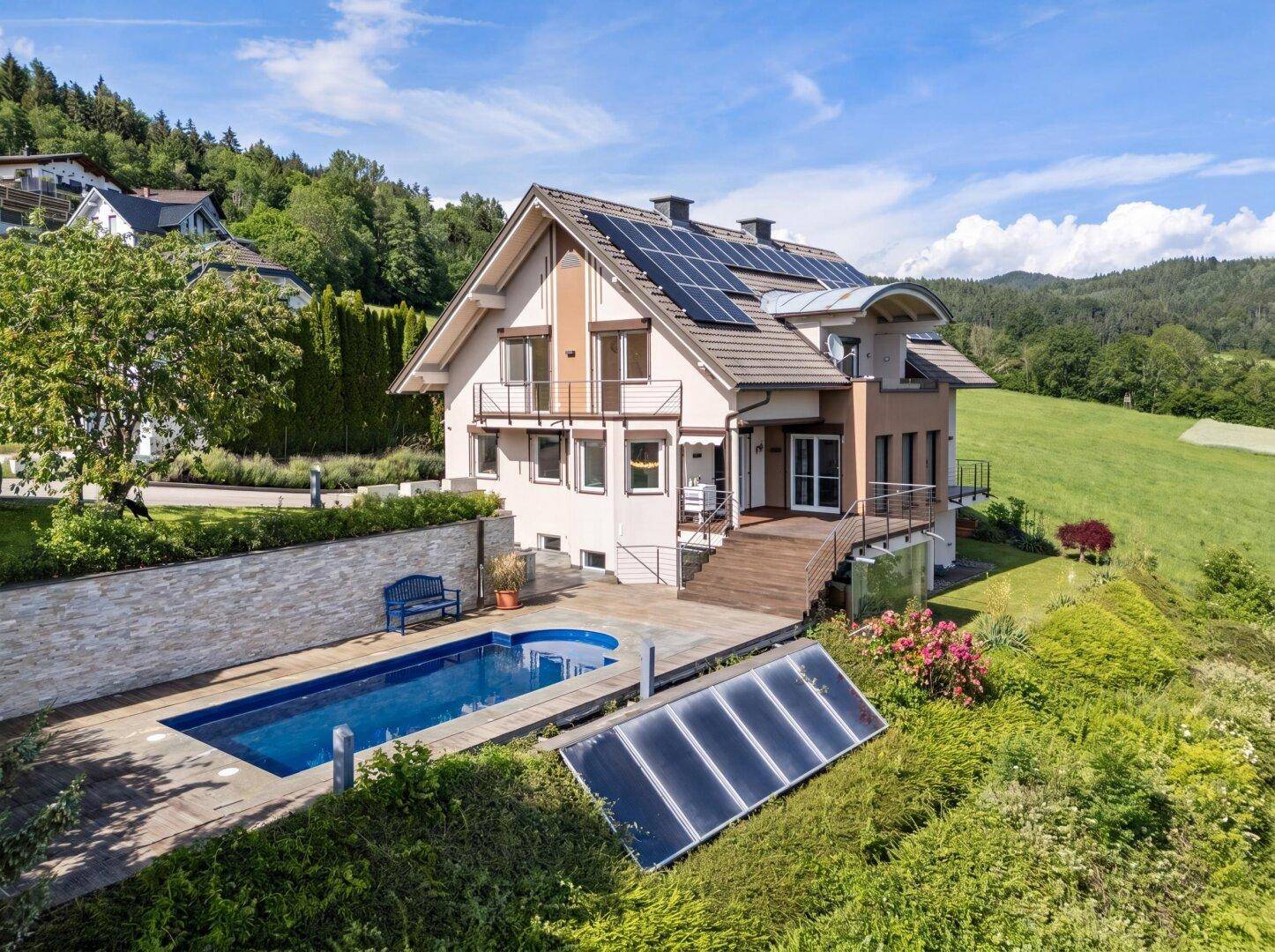 Luftaufnahme eines Hauses mit Pool, Solaranlagen auf dem Dach und weitem Blick ins Grüne.