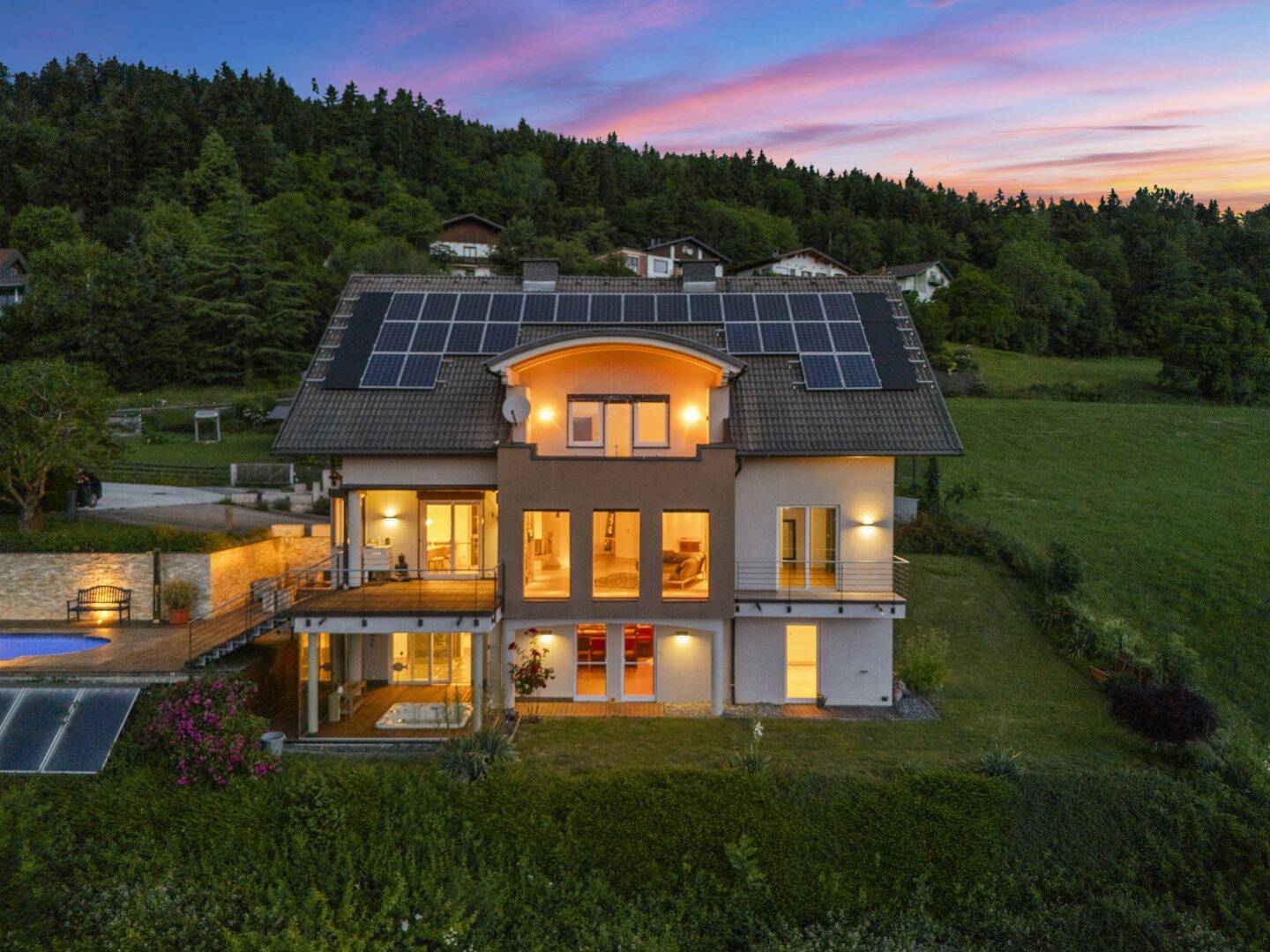 Luftaufnahme des Hauses mit Pool und Solaranlagen, beleuchtet unter einem farbenfrohen Abendhimmel.