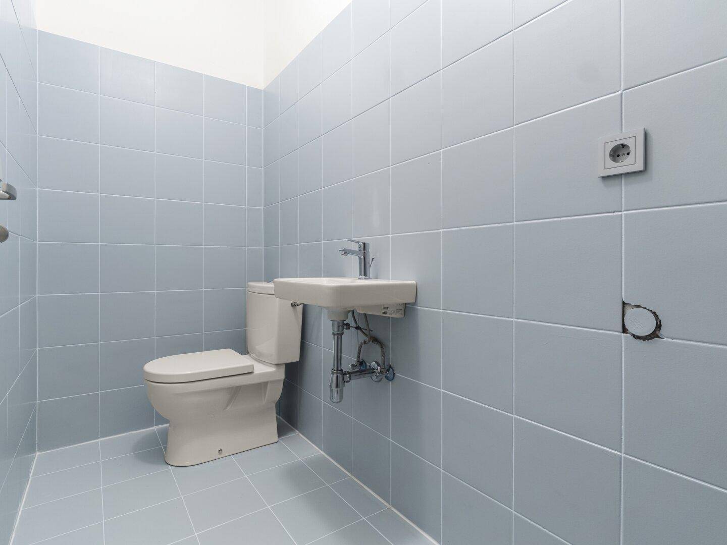 Kleines, hellblau gefliestes Gäste-WC mit Toilette und Waschbecken, funktional eingerichtet.