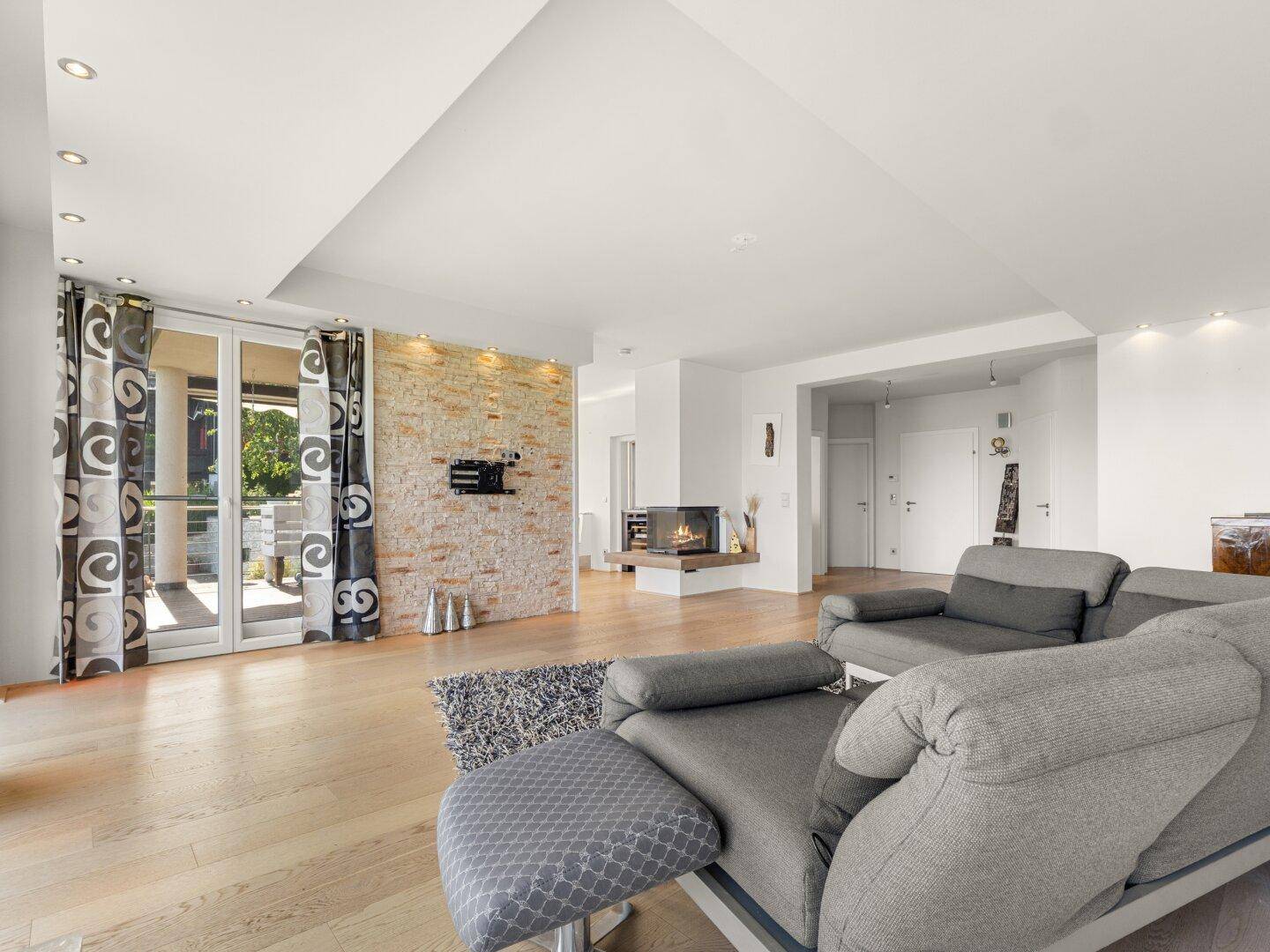 Geräumiges Wohnzimmer mit Holzboden, Kamin und Zugang zu einer Außenterrasse.