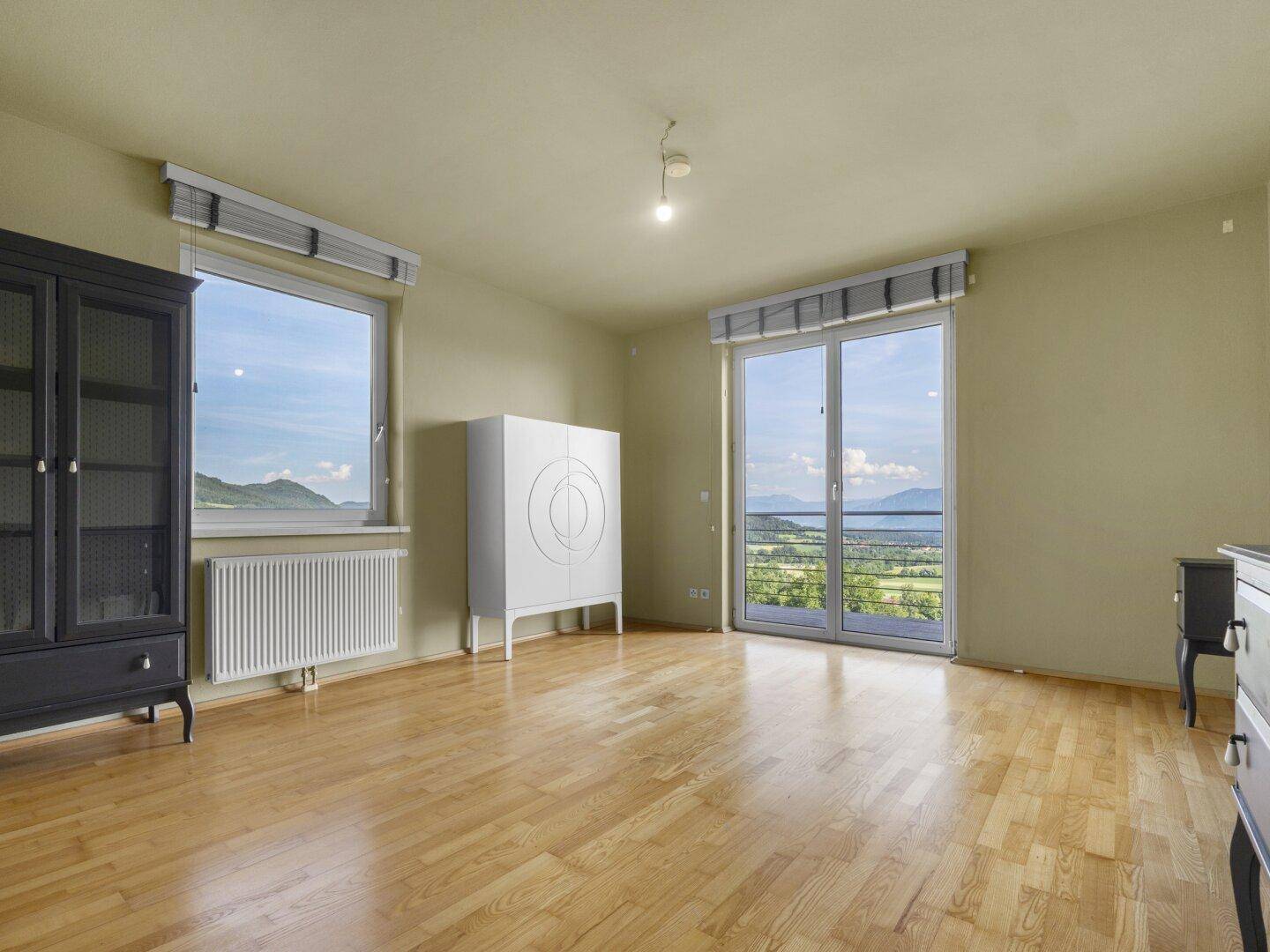 Helles Schlafzimmer mit Holzboden, Balkonzugang und malerischem Landschaftsblick.
