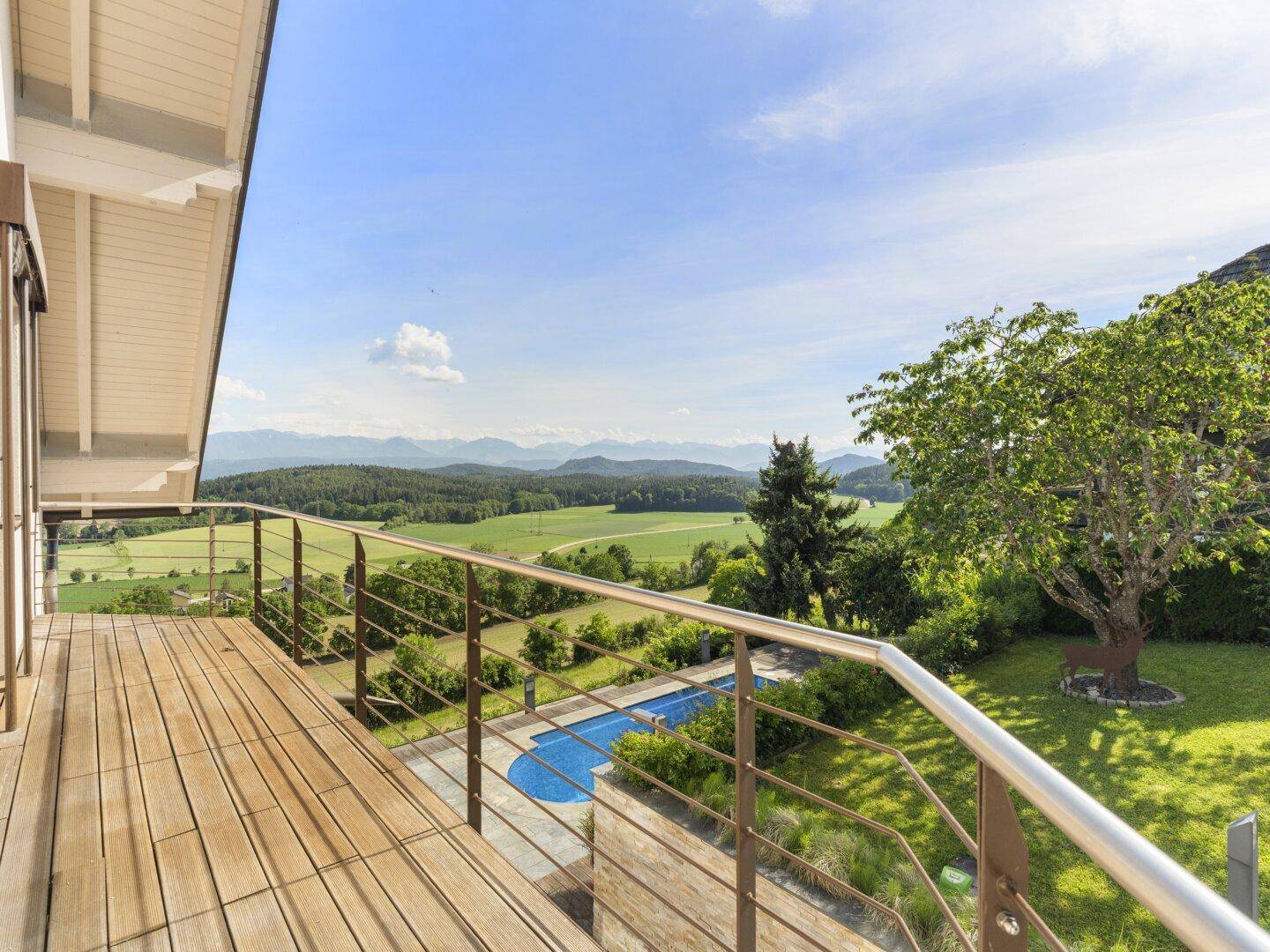 Großer Holzbalkon mit Glasgeländer, Panoramablick auf Berge und Pool.