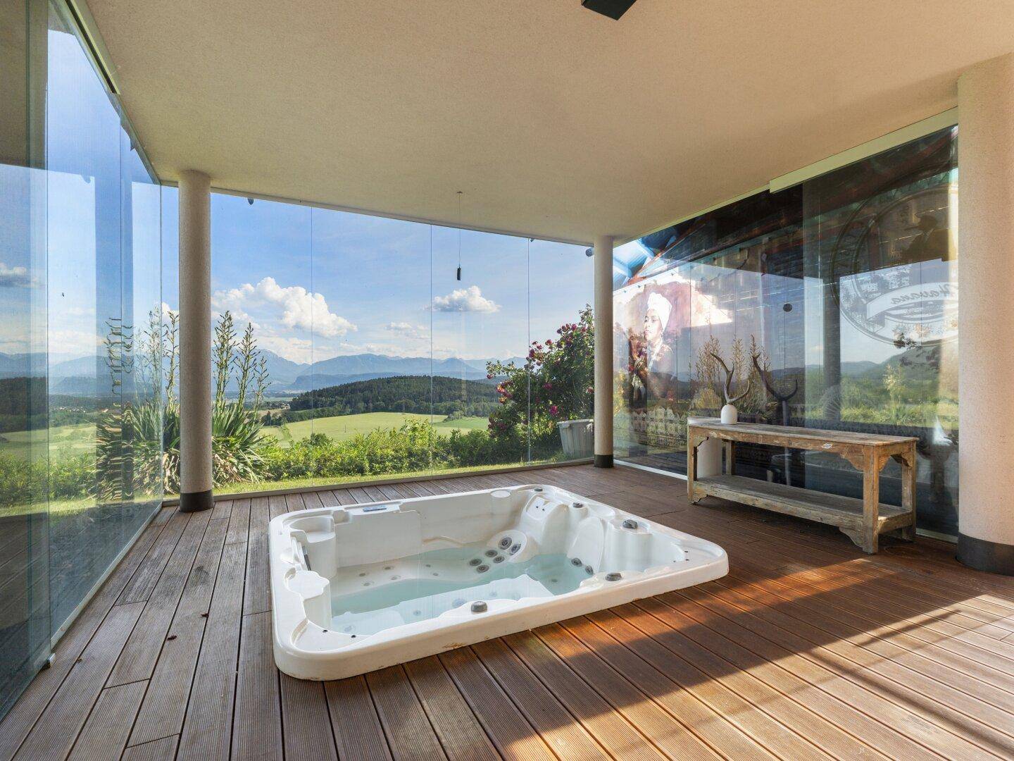 Entspannungsbereich mit Whirlpool auf der Holzterrasse, umgeben von Glas und Natur.