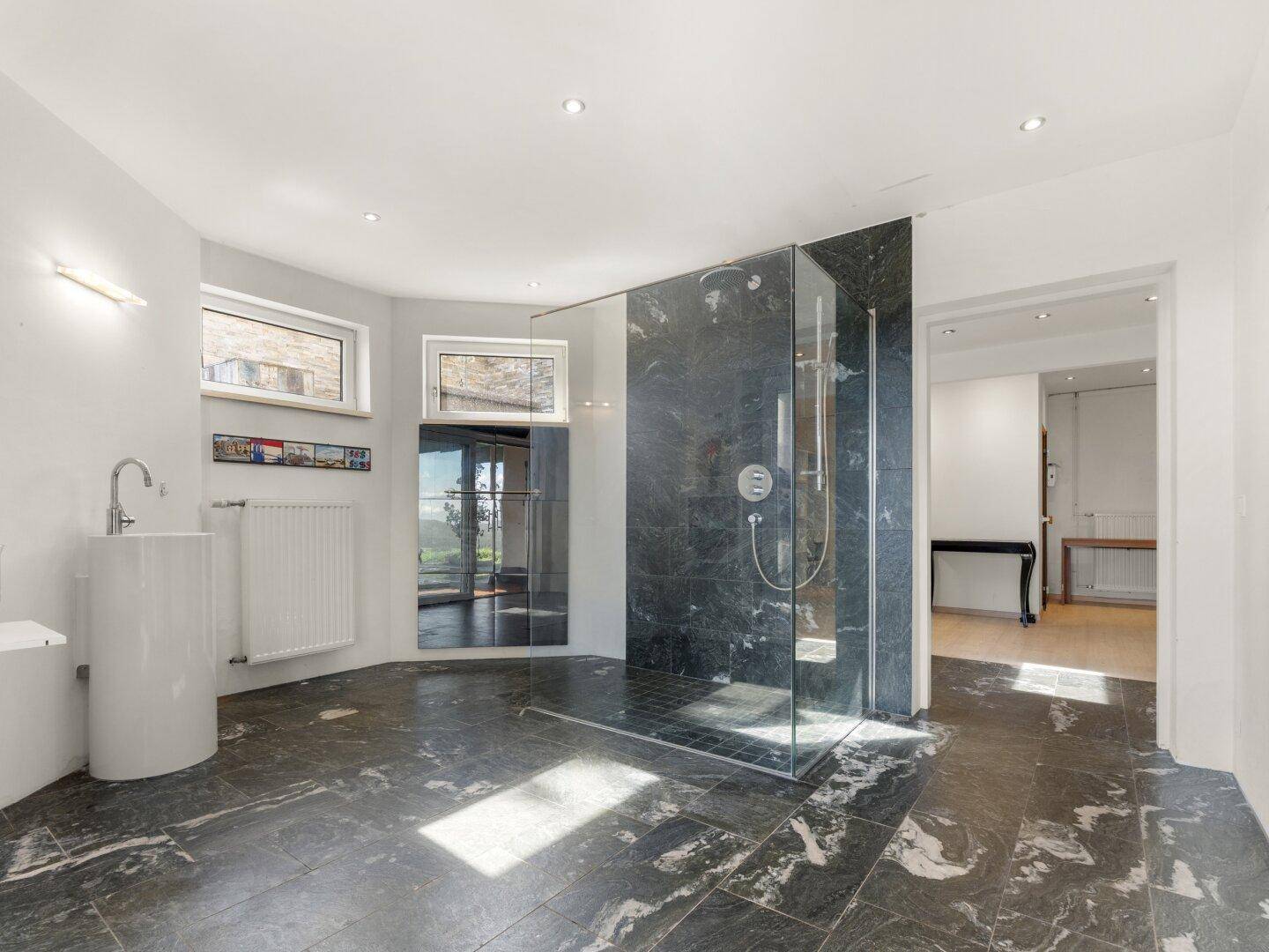 Geräumiges Badezimmer mit moderner begehbarer Dusche und dunklem Natursteinboden.