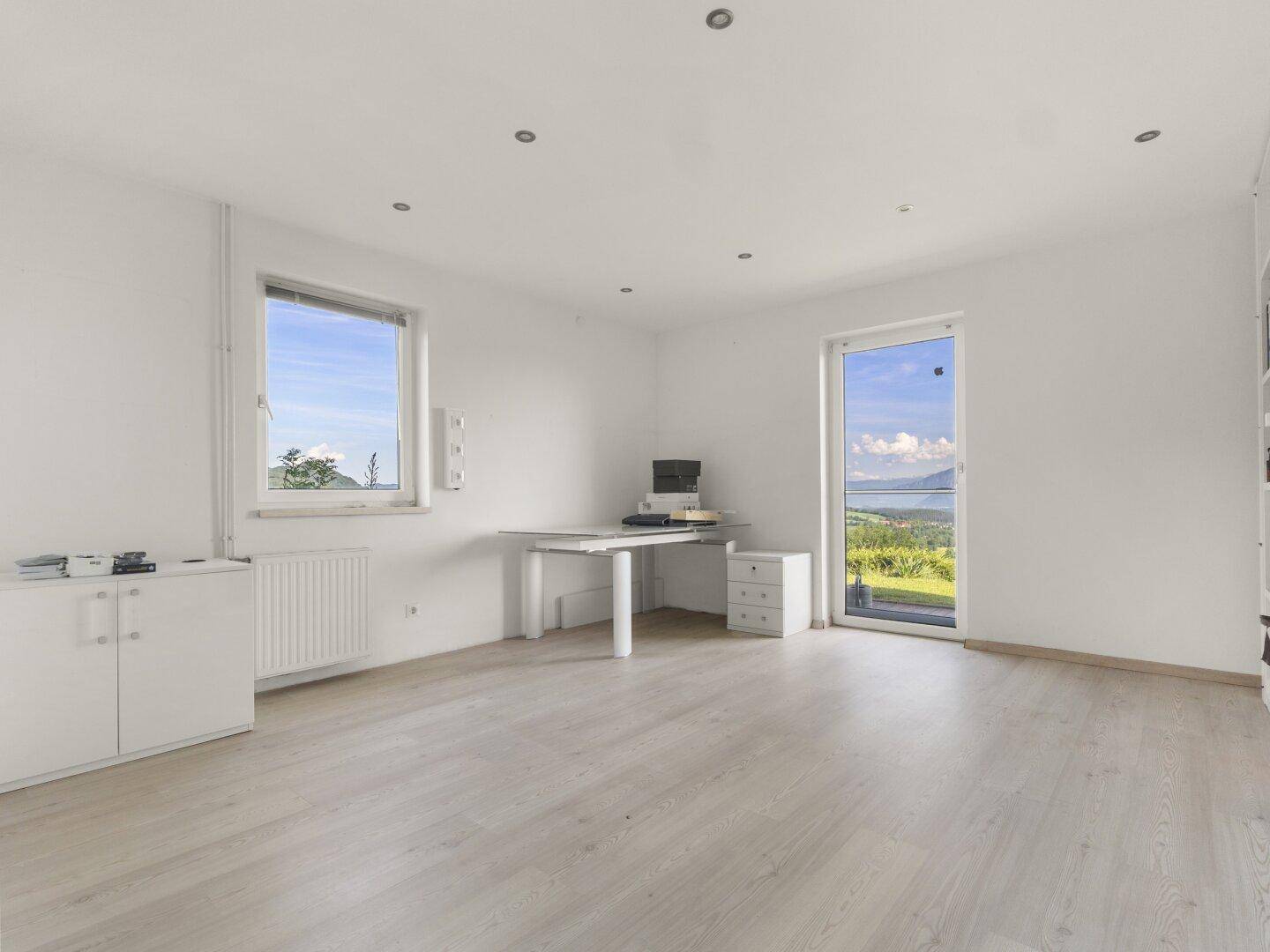 Helles Arbeitszimmer mit weiß gestrichenen Wänden, Holzboden und weitem Ausblick.