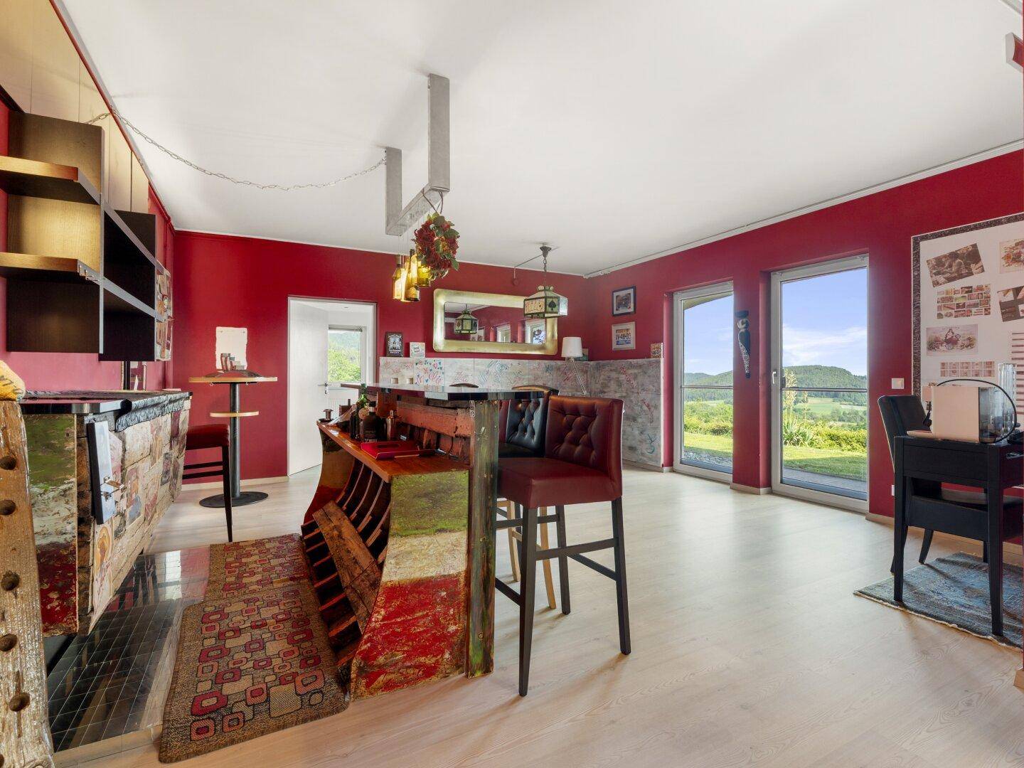 Farbenfroher Wohnbereich mit Bar, roten Wänden und Zugang zu einer Terrasse mit Aussicht.