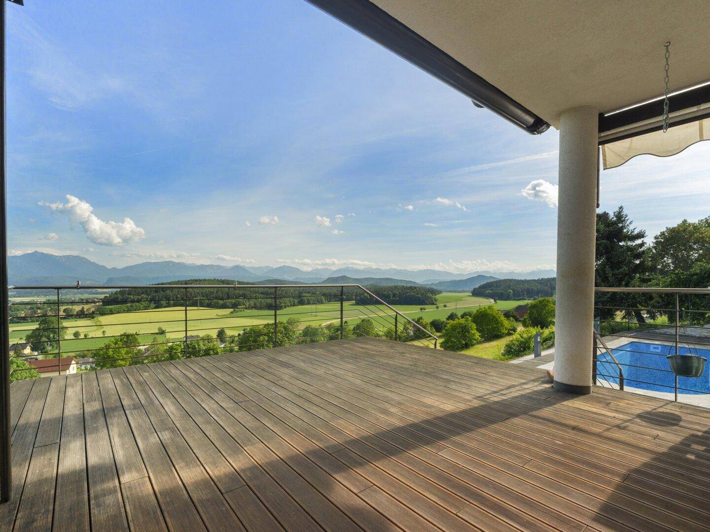 Große Holzterrasse mit Überdachung, Poolzugang und weitem Blick auf die Berge.