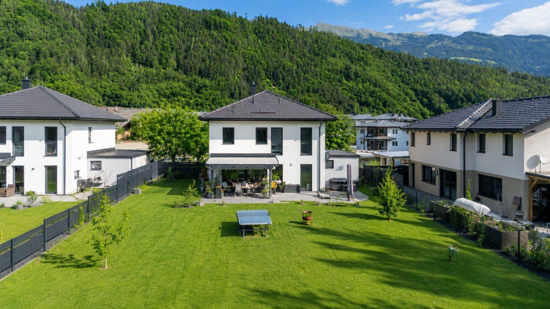 Großzügiger Garten mit Rasenfläche und überdachter Terrasse vor der modernen Villa.