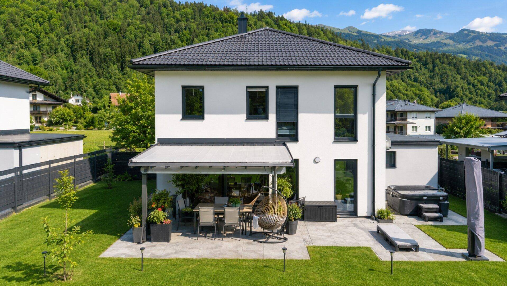 Hinterhof mit großer Rasenfläche, überdachter Terrasse und Whirlpool mit Bergblick.