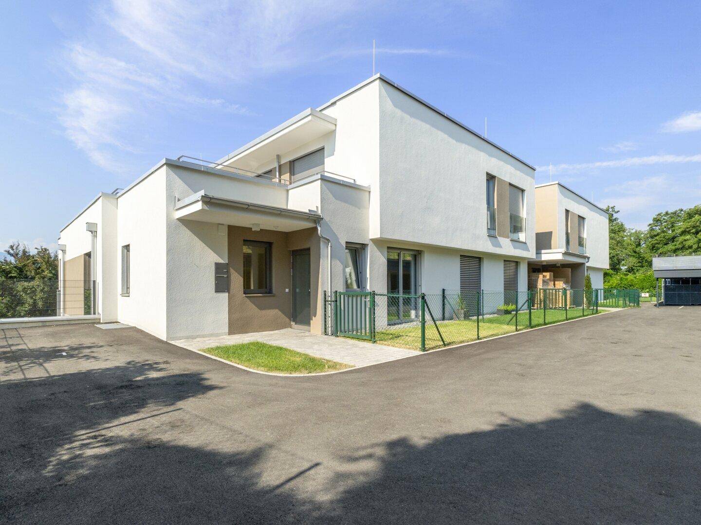 Moderne Wohnanlage mit weißer Fassade, kleinen Vorgärten und gepflastertem Eingangsbereich.