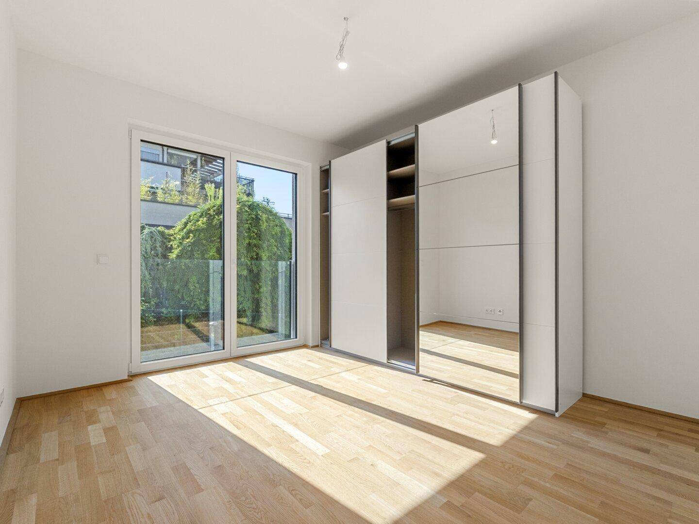 Helles Schlafzimmer mit Parkettboden, großem Einbauschrank und Zugang zum Außenbereich.