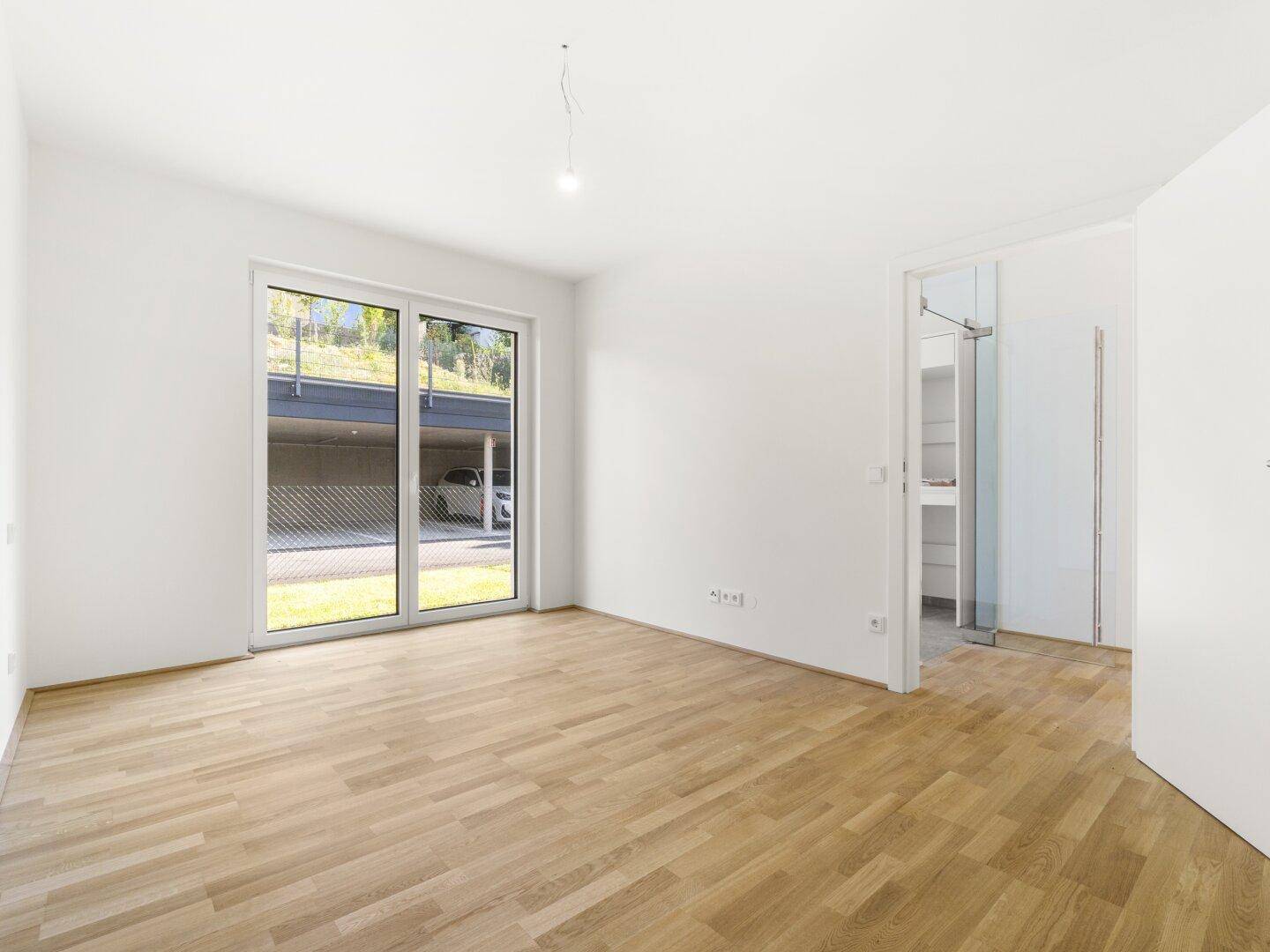 Helles Schlafzimmer mit Eichenparkett, großen Schiebetüren und Zugang zu einem begehbaren Kleiderschrank.