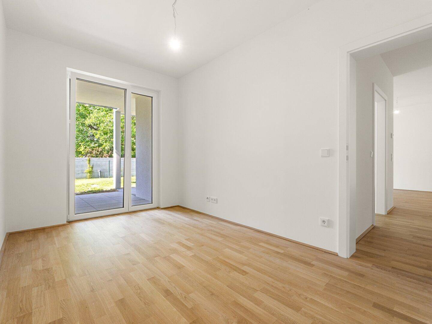 Heller, leerer Raum mit Holzboden und großen Schiebetüren, die zu einem Außenbereich führen.