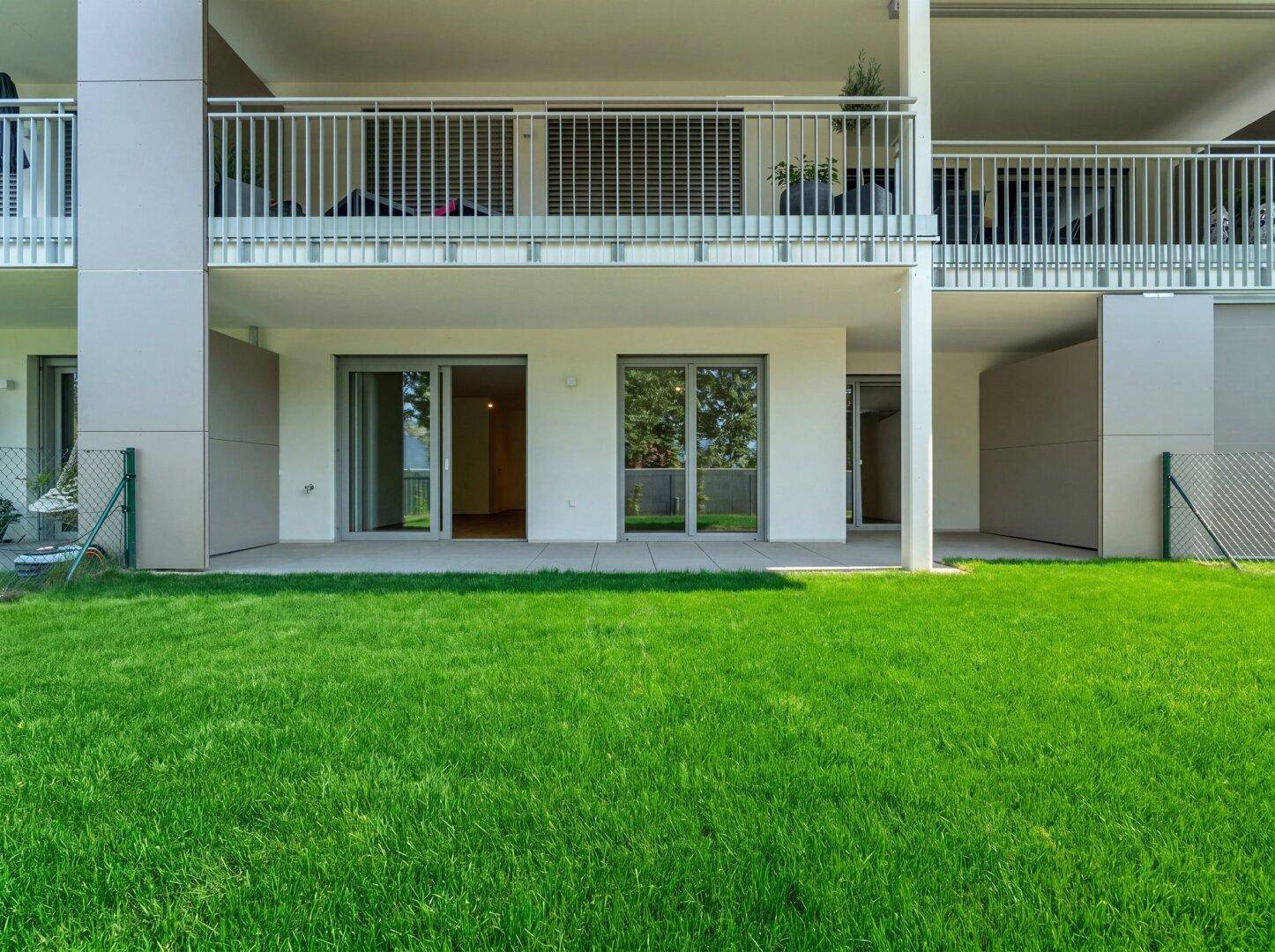 Erdgeschossfassade eines modernen Gebäudes mit großen Glasfronten und direktem Zugang zu einem grünen Garten.