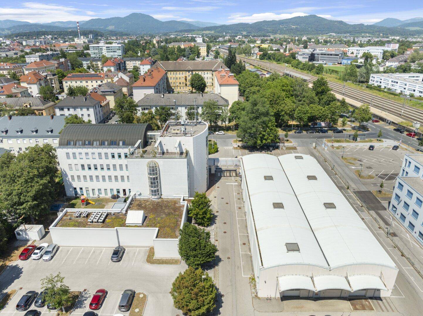 Weitläufige Luftaufnahme des Gewerbegebiets mit Gebäuden, Parkplätzen und Bahngleisen im Hintergrund.
