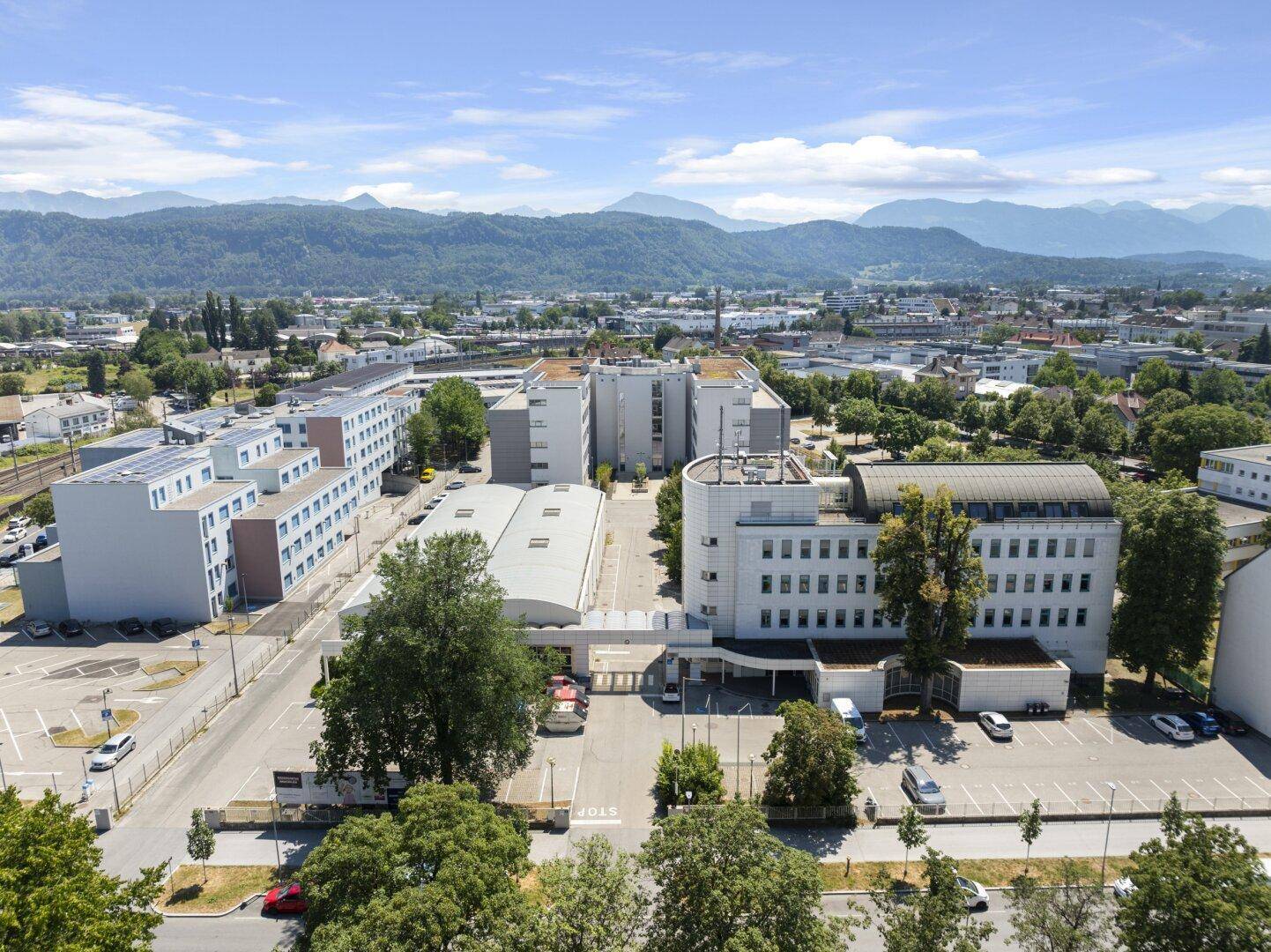 Weitläufige Luftaufnahme des Gebäudekomplexes und der umliegenden Stadtlandschaft mit Bergen im Hintergrund.