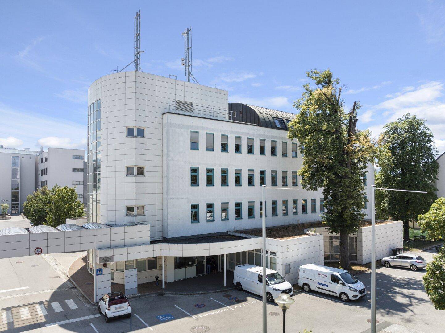 Moderne Bürogebäude-Fassade mit markanter Architektur, Eingangsbereich und Parkplätzen.
