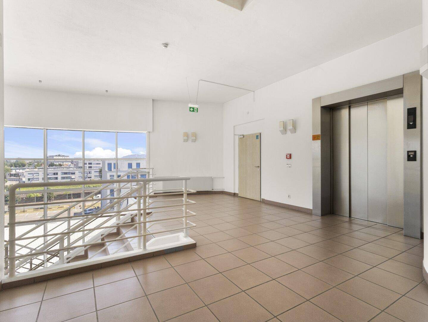 Heller Treppenabsatz im Obergeschoss mit Fliesenboden, Aufzug und weitem Blick über die Stadt.