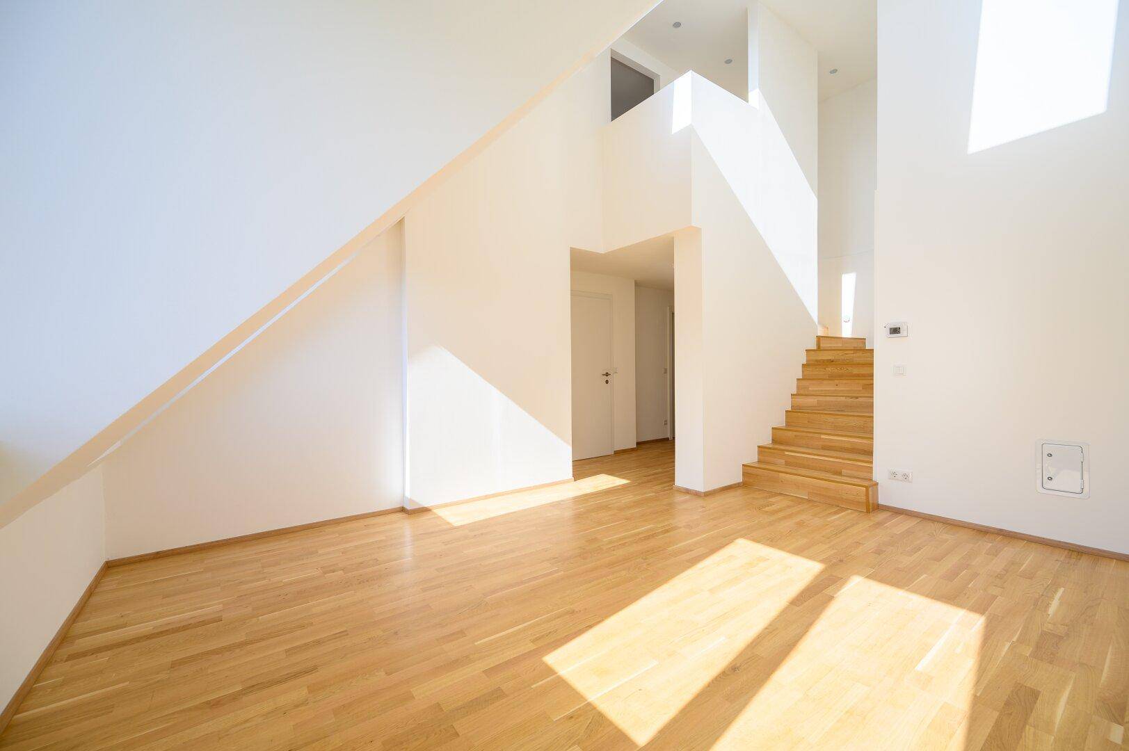 Geräumiges, lichtdurchflutetes Zimmer mit Holzparkett und moderner Holztreppe, ideal für offenes Wohnen.