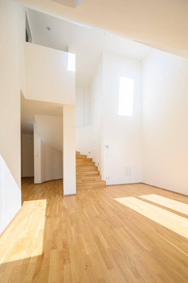 Heller Wohnbereich mit Eichenparkett, hohen Decken und einer stilvollen Holztreppe, die zum Obergeschoss führt.