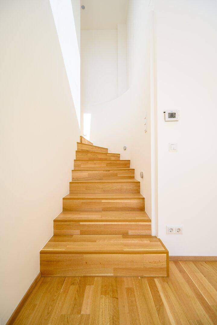 Elegante Holztreppe mit hellen Stufen und weißen Wänden, die natürliches Licht einfängt.