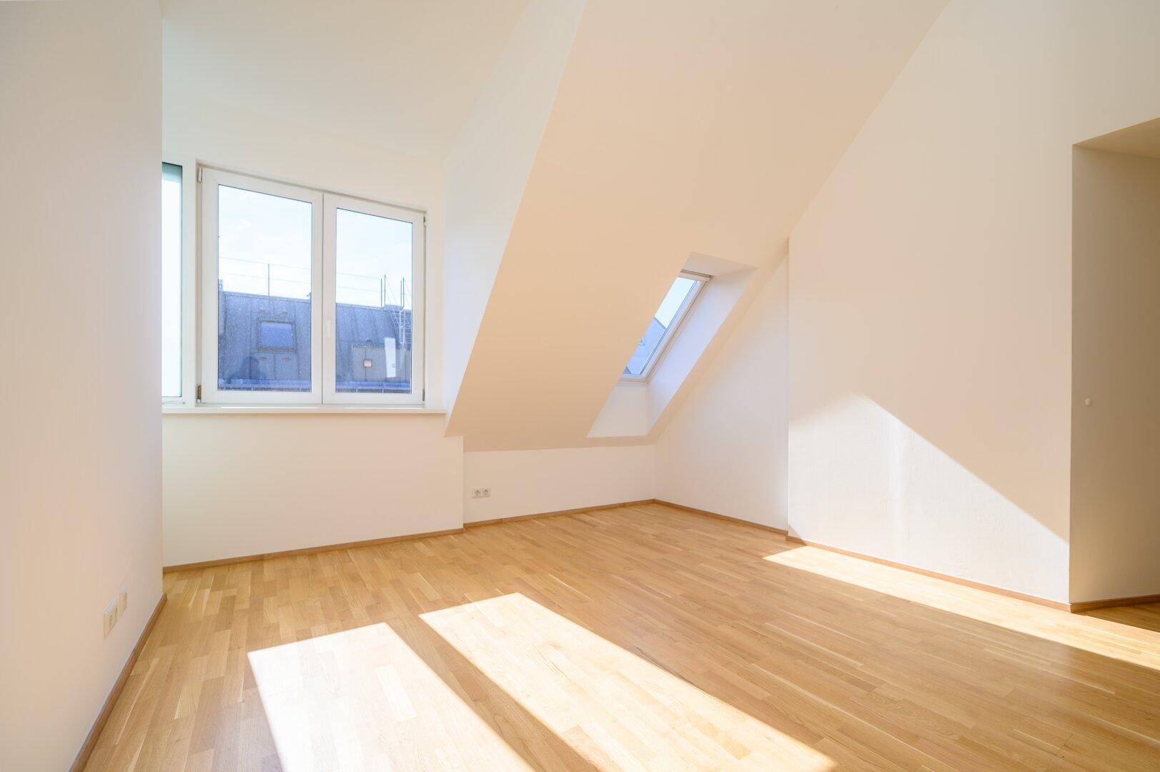 Helles Zimmer im Dachgeschoss mit Holzparkett, großem Fenster und zusätzlichem Dachfenster für viel Licht.