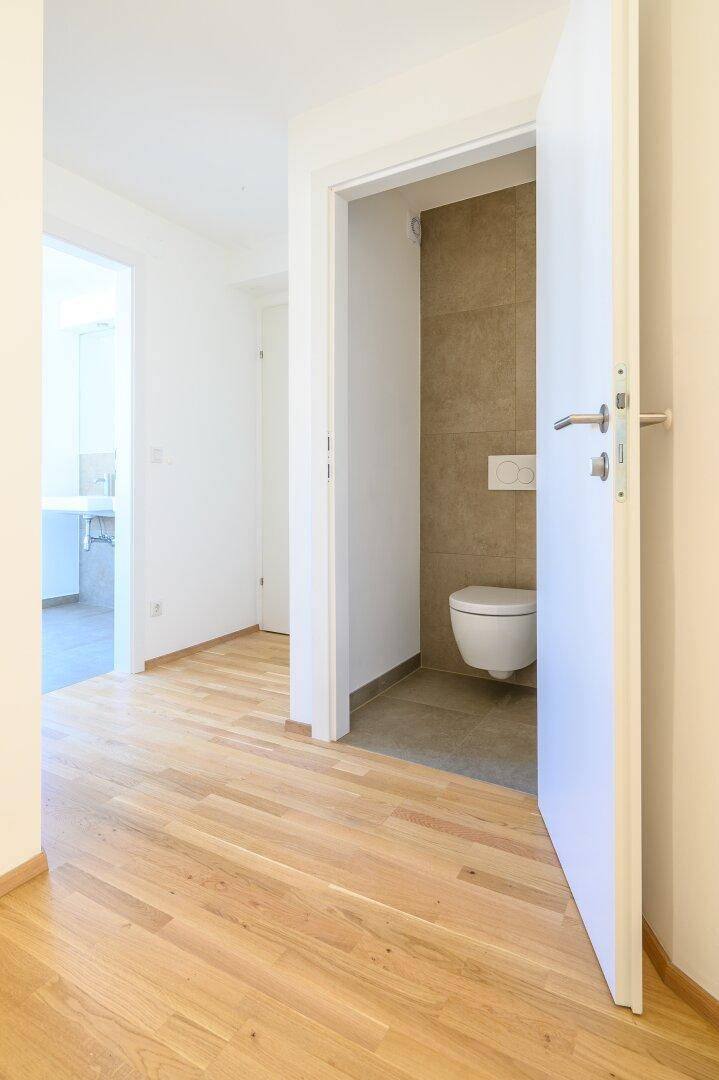 Flur mit Holzparkett und Zugang zu einem modernen Gäste-WC mit Wand-WC und neutralen Fliesen.