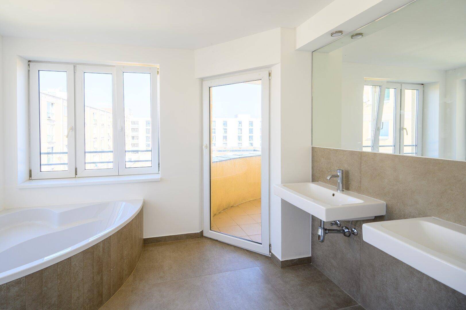 Modernes Badezimmer mit Eckbadewanne, Doppelwaschbecken, großem Fenster und direktem Zugang zum Balkon.