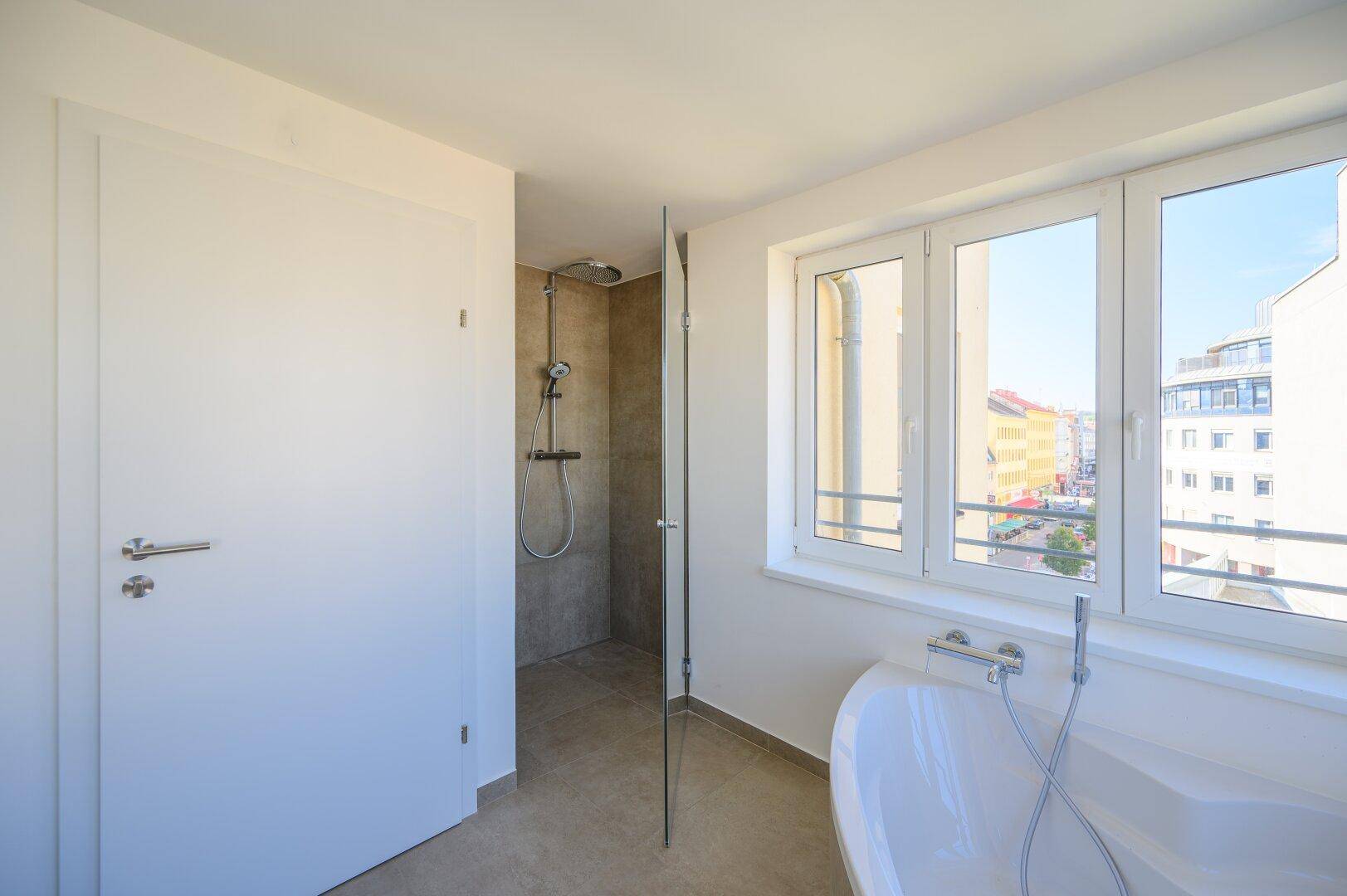 Helles Badezimmer mit begehbarer Dusche, Badewanne und großem Fenster, das viel Tageslicht hereinlässt.