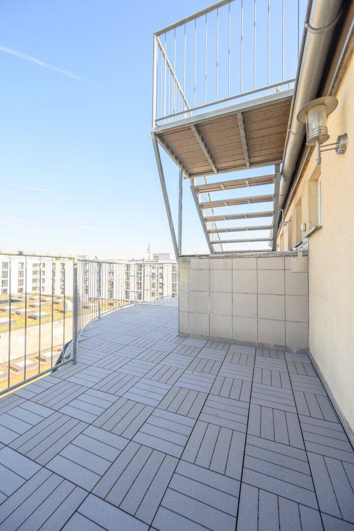 Geräumige Dachterrasse mit modernen grauen Fliesen, Metallgeländer und Blick über die Stadt.