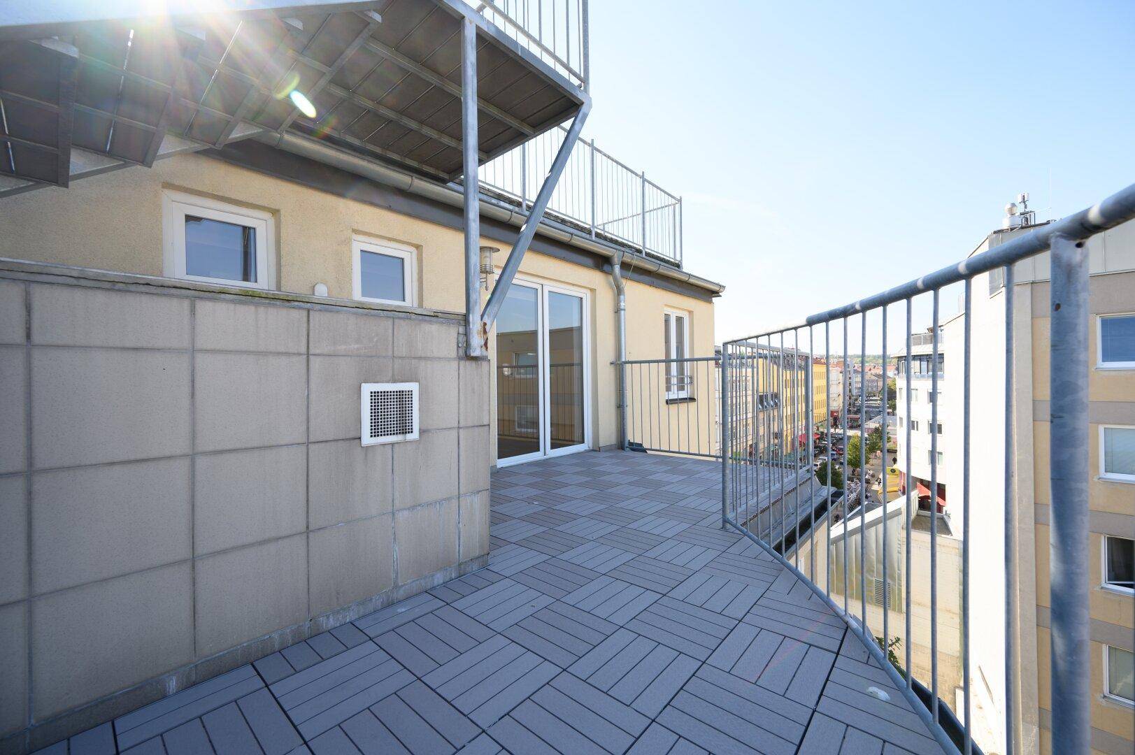 Weitläufige Terrasse mit grauen Bodenfliesen und Metallgeländer, bietet einen Panoramablick auf die Stadt.