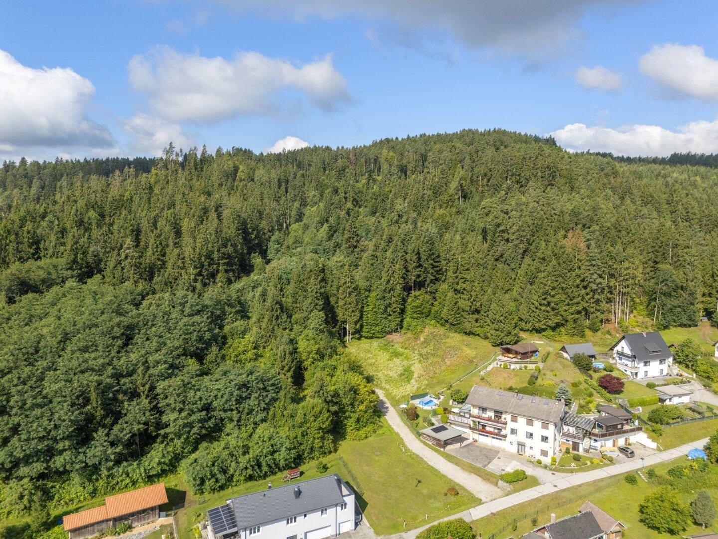 Panoramablick aus der Vogelperspektive auf bewaldete Hügel und einige Wohnhäuser in der Natur.