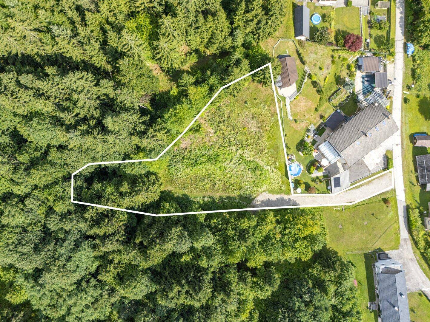 Senkrechte Luftaufnahme eines umrandeten Grundstücks, umgeben von Wald und angrenzenden Häusern.