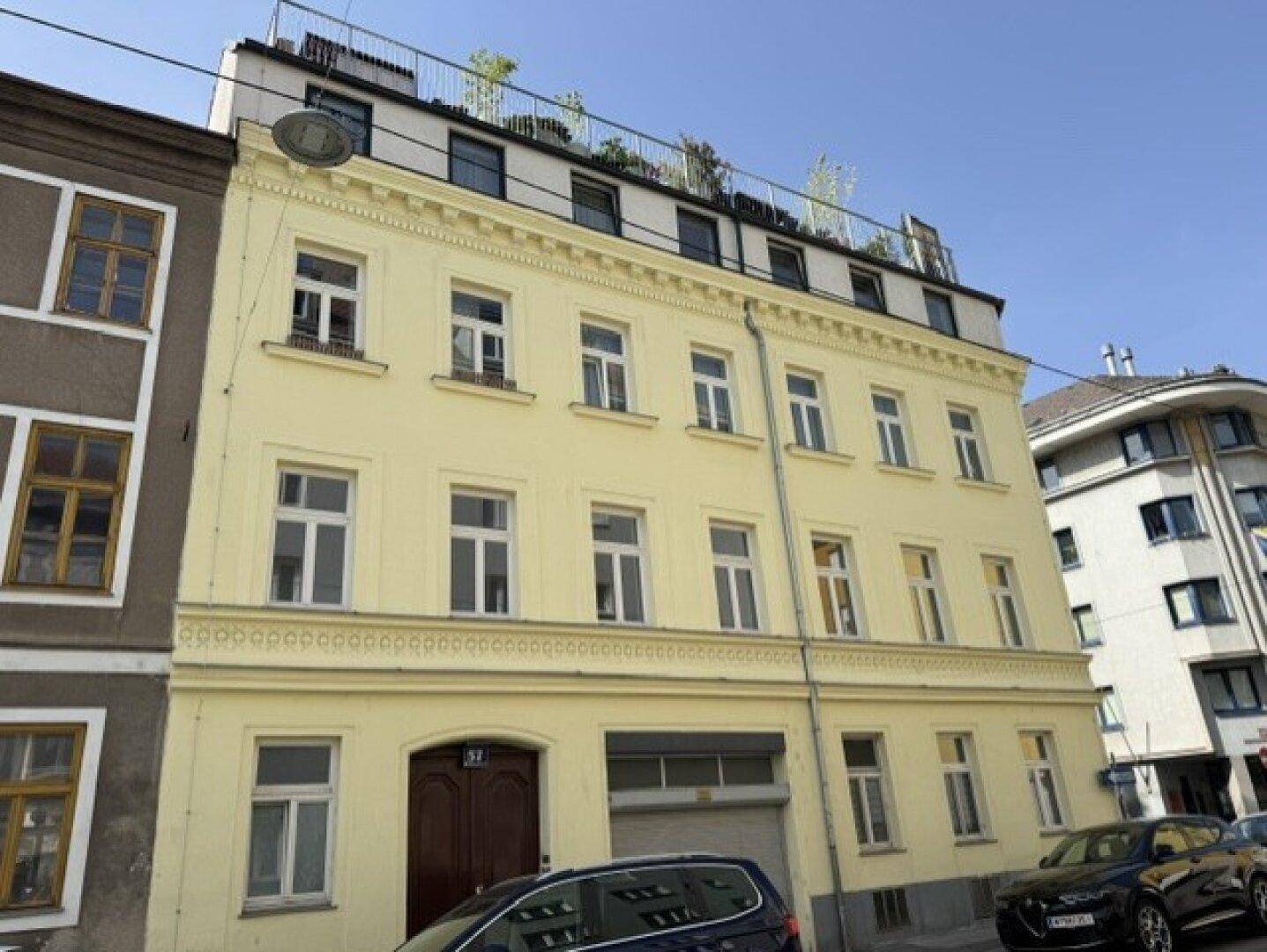 Historisches Gebäude mit gelber Fassade und begrünter Dachterrasse.