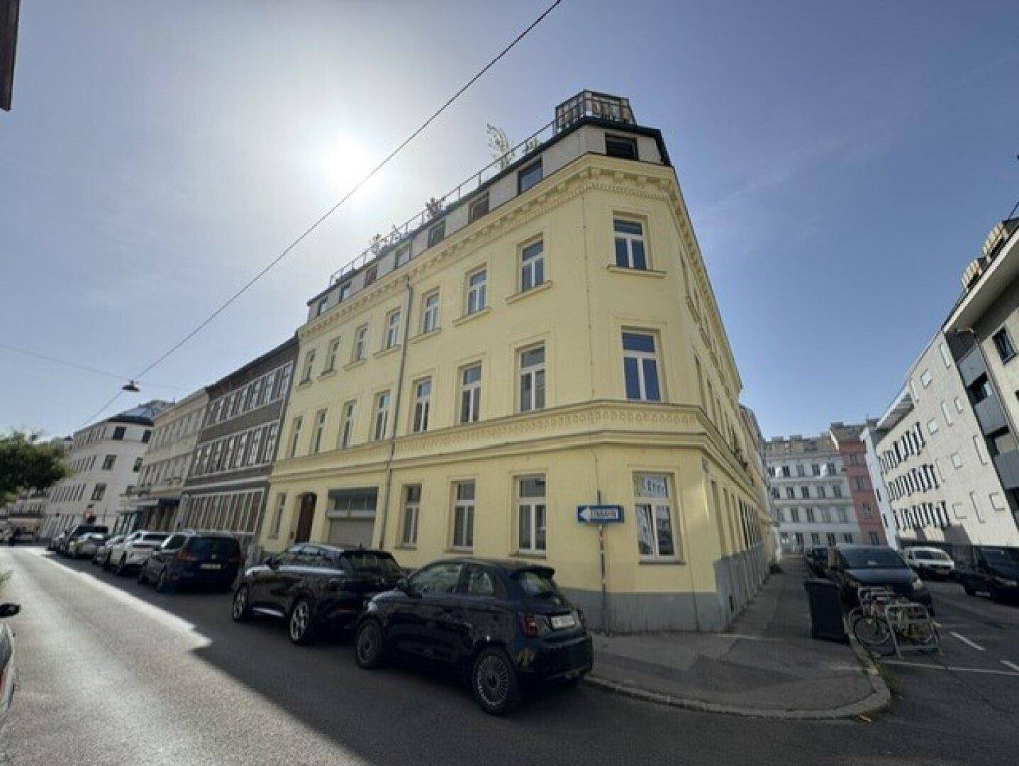 Historisches Eckgebäude mit gelber Fassade und moderner Dachterrasse in urbaner Umgebung.