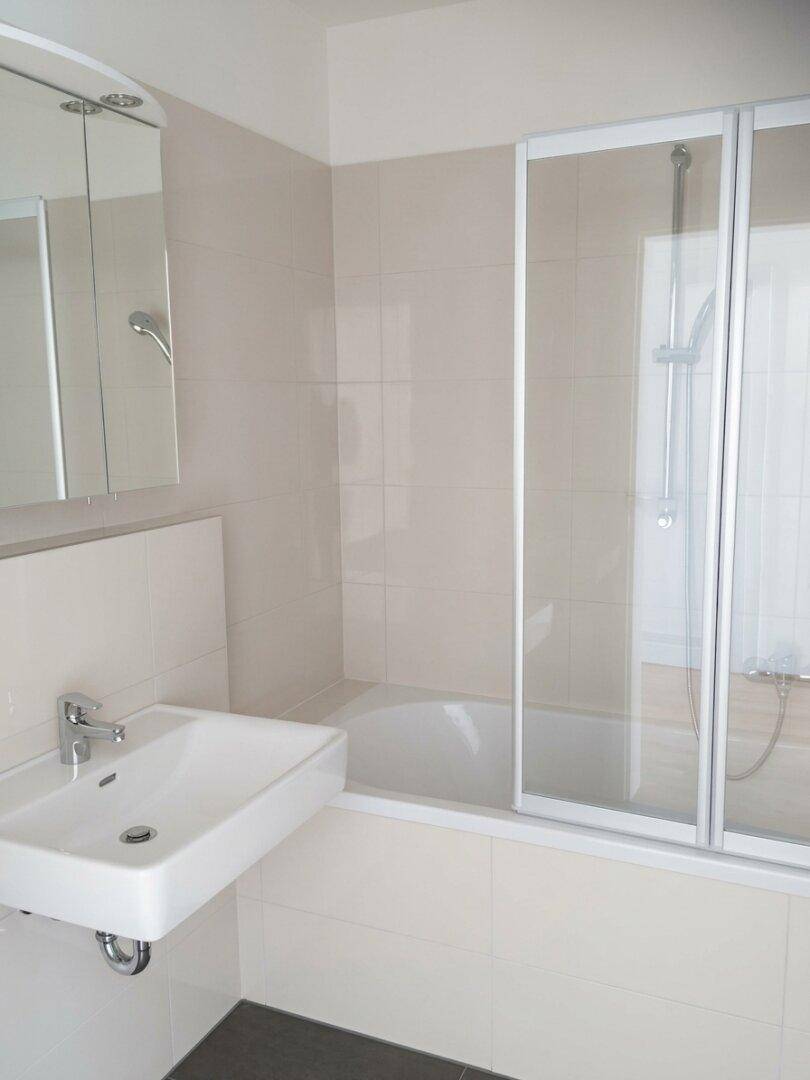Helles Badezimmer mit Badewanne, Duschabtrennung und modernem Waschbecken.