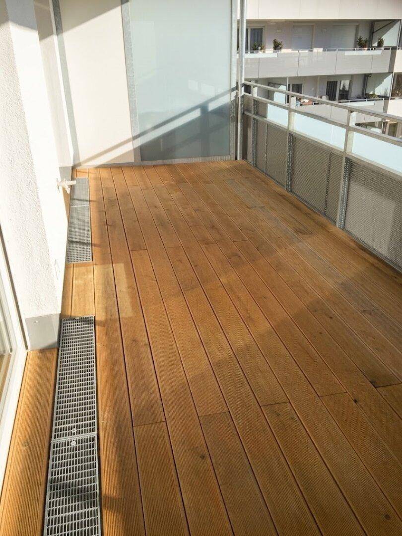Geräumiger Balkon mit Holzboden und moderner Glasbrüstung, ideal für Entspannung im Freien.