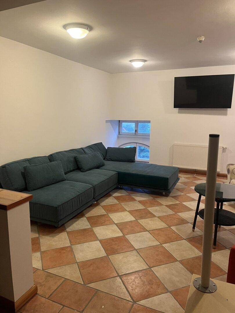 Gemütliches Wohnzimmer mit großem Ecksofa, Fliesenboden und kleinem Fenster.