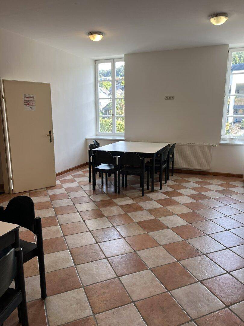 Heller Essbereich mit großem Tisch, Stühlen und kariertem Fliesenboden.