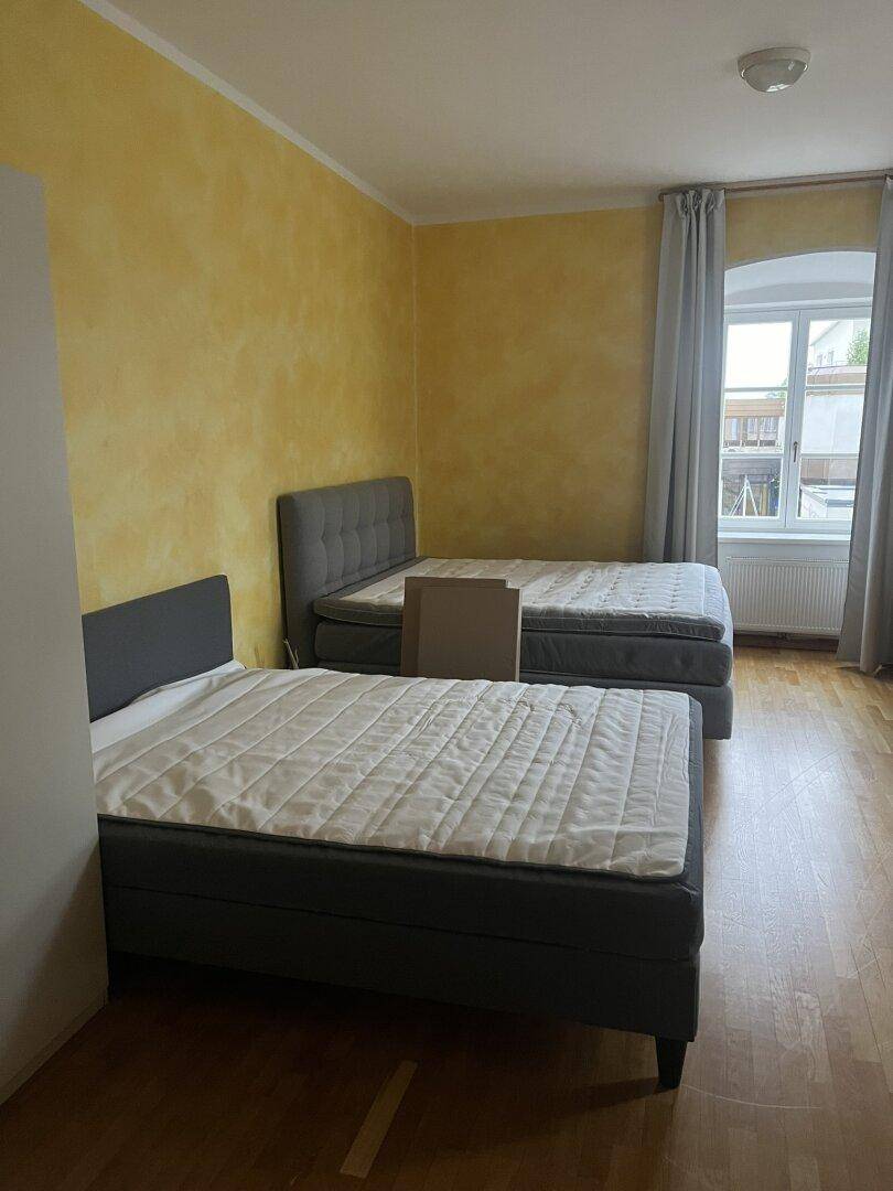 Schlafzimmer mit zwei Einzelbetten, Holzboden und gelb gestrichenen Wänden.