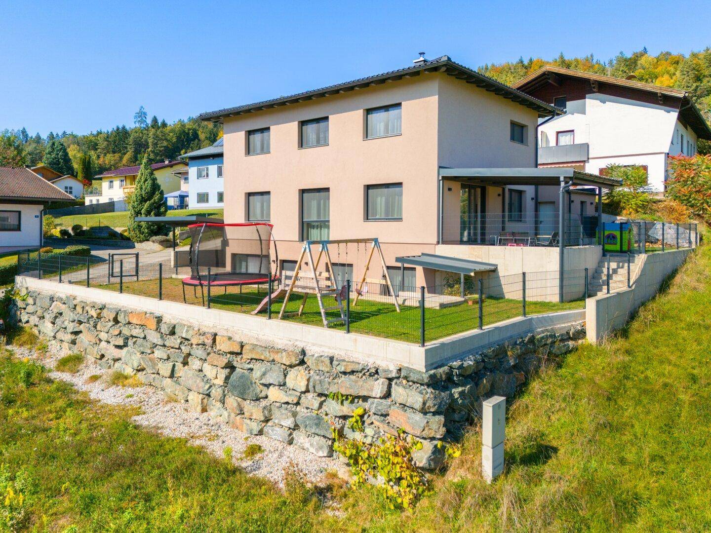 Rückansicht des Hauses mit eingezäuntem Garten, Spielplatz und Trampolin.