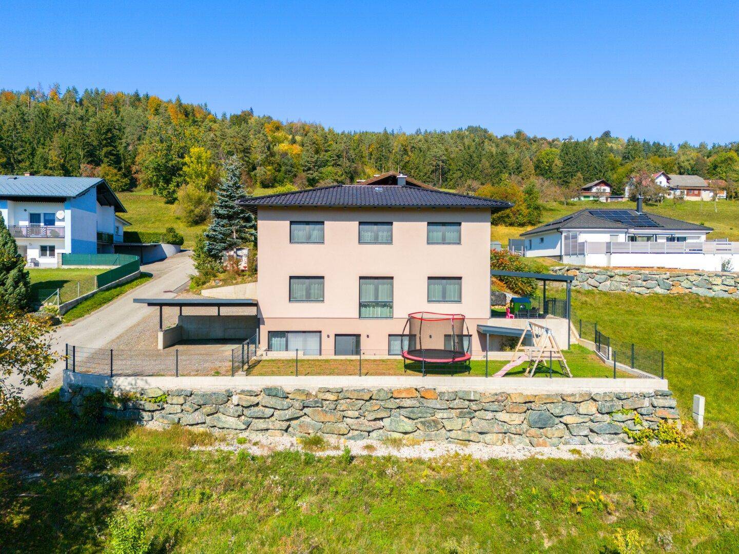 Ansicht des Hauses mit Garten, Trampolin und Spielplatz in grüner Umgebung.