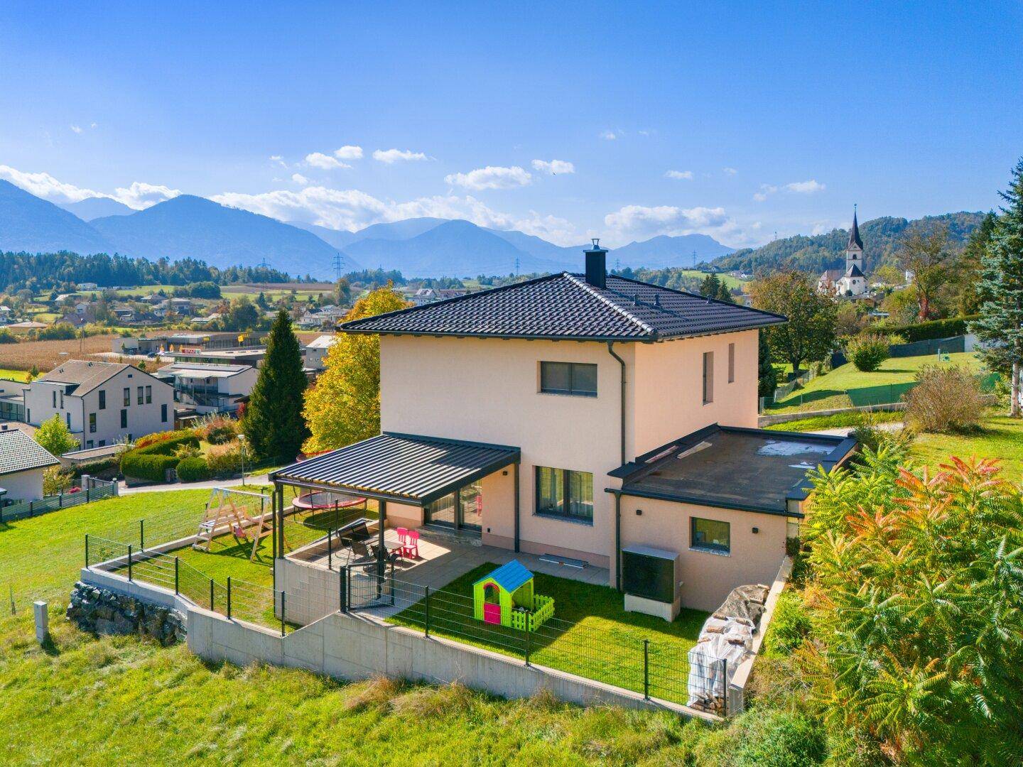 Luftaufnahme des Hauses mit Garten, Spielbereich und Bergblick in ländlicher Umgebung.
