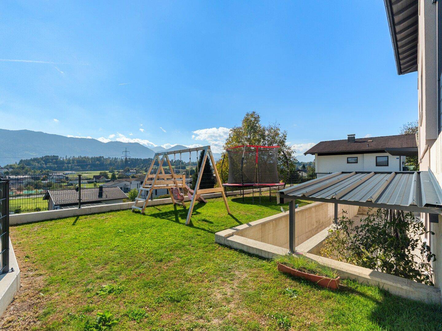 Grüner Gartenbereich mit Schaukel, Trampolin und weitem Bergblick.