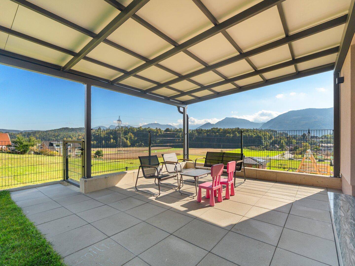 Überdachte Terrasse mit Sitzgelegenheiten und weitem Blick auf die Berge.